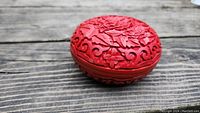 Oval-shaped red Chinese cinnabar lacquerware box carved with intricate floral and leaf patterns on wooden surface.