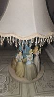 Photo showing the lamp with beige fabric shade and Disney princess figurines on the base in front of a castle structure.