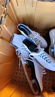 Two pairs of white figure skates inside a storage bin, showing the left and right boots with laces and metal blades visible.