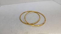 Two gold tone bangles on a white surface, showing general shape and decoration.