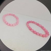 Two handmade rose quartz stretch bracelets displayed on a white surface, showing the different pink shades of the beads.