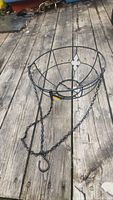Full view of the black iron hanging plant basket with attached chains and hook, sitting on wooden planks.