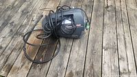 Photo showing black pressure washer with power cord and hose coiled around it, placed on a wooden deck.