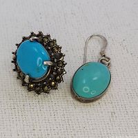 Close-up photo showing both earrings; one with turquoise surrounded by marcasite stones in silver setting, the other a simple oval turquoise stone in silver hook design.