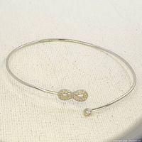Photo of sterling silver open bangle bracelet showing infinity symbol and single stone ends on light fabric background.