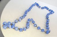 Front view of blue and white marbled bead necklace laid out on a light fabric background.