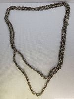 Full view of the very large vintage chain necklace laid flat on white fabric backdrop, showing intertwined rope-style links and length.