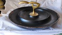 Side view of the vintage brass nutcracker mounted on a black round tray showing wear and paint chipping.