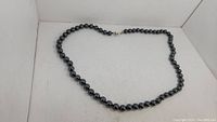Full view of vintage magnetite bead necklace laid out in curve shape showing glossy dark spherical beads and clasp.