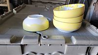 Four stacked yellow and floral ceramic bowls plus one bowl upside down showing yellow exterior and white interior.