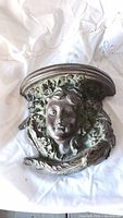 Decorative wall bracket with cherub face and floral details lying on a white fabric.