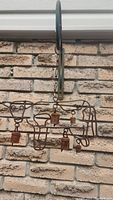 Full view of the metal cow-shaped wind chime with hanging bell elements affixed to a brick wall.