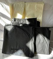 Photo showing three black garment bags stacked with clear window tag and a beige garment bag behind them