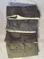 Top view of four men's dress pants folded showing buttoned rear pockets and inner lining color contrast.
