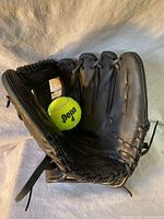 Front open view of black Easton BL1150 baseball glove showing interior pocket and lacing; a yellow tennis ball used for size comparison is placed inside.