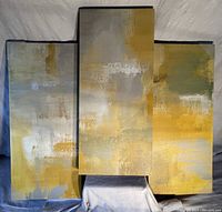 Three abstract art canvas wall panels in silver, gold, yellow, grey and white tones displayed vertically together showing texture and color tones.