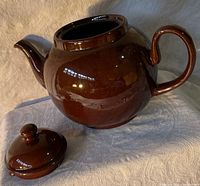 Chestnut brown ceramic teapot with lid placed in front, showing general shape and size.