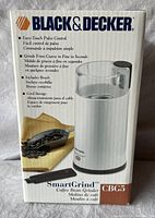 Box front showing Black & Decker branding, model Smart Grind CBG5, highlights pulse control, grind range, includes brush and cord storage, and photo of the grinder with coffee beans.