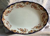 Top view of oval decorative serving platter showing floral and blue scalloped rim with white center