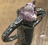 Close-up of silver ring with pink heart-shaped cubic zirconia center and small white cubic zircons on band, showing front angle.