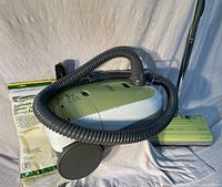 Full view of Kenmore canister vacuum with flexible black hose, olive green and white body, and included disposable vacuum bags.