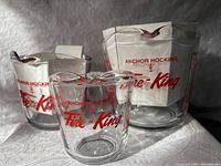 Three clear glass measuring cups with red Fire-King logo and measurements, arranged with the smallest cup in front and largest behind.