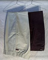 Two pairs of chinos folded and hung on hangers, showing dark brown and light tan colors and overall condition