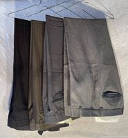 Four men's dress pants hung together showing colors and fabric texture, folded at the knee area
