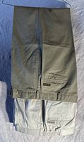 Pair of khaki beige Savane chino pants folded, showing back pocket with button and belt loops