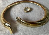 Photo of the gold tone plated corrugated choker necklace with clip-on lock and topaz encrusted ring placed on fabric background.