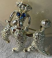 Front view of detailed silver tone poodle brooch with sapphire gem eyes showing texture and color.