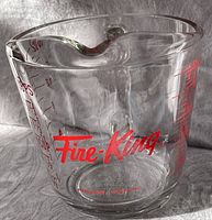 Clear glass measuring cup with red Fire-King logo on front, no visible damage.