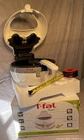 T-fal ActiFry air fryer open showing interior paddle, resting on original foam packaging with measuring tape for scale.