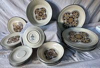 Overview of dinnerware set arranged showing stack of large plates, medium and small plates, and bowls with clear view of medallion design.