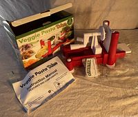 Manual vegetable slicer and fruit peeler with crank handle, suction feet, three blades, instruction manual and original packaging. Box lip slightly bent.
