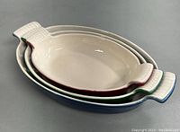 Three enamelled cast iron oval dishes nested together showing cream interior and colored exteriors in red, green, and blue.