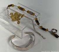 Four pieces: sterling silver cuff bracelet, sterling silver chain bracelet, toggle clasp bracelet with amber and brown beads, and a flower-shaped sterling brooch.