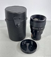 Mosty Anamorphic Adaptor SE lens next to its black carrying case and lens cap on a white surface.
