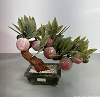 Side view of the Chinese jade bonsai tree sculpture showing its brown trunk, green jade leaves, and pink jade fruits in a rectangular jade pot with white stones.