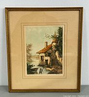 Frontal image of framed etching featuring a rustic stone building with turret and stairs beside a pond, under light blue sky with trees.