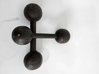 Top view of a dark, handmade cast iron dumbbell showing three spherical weights connected by solid handles forming a tripod design.