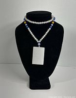Full front view of necklace on black display stand showing white jade pendant and beaded necklace.