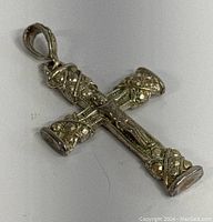 Metal crucifix pendant showing embossed Christ figure and decorative floral and swirl motifs on cross arms, lying flat on background.