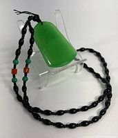 Full view of the natural green jade pendant hanging from the black beaded chain showing size and color contrast.