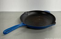 Blue enamelled cast iron frying pan with dual pouring spouts and blue handle lying flat showing interior surface.