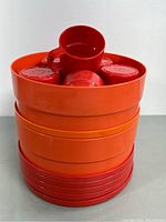 Stacked view of the red cups inside the orange bowls and plates, showing the size and finish of each item.