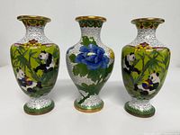 Front view of three brass cloisonné vases with panda and floral designs, showing detailed enamel work.