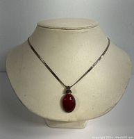 Necklace displayed on a stand showing the oval amber pendant and flat woven chain.