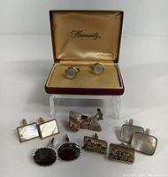 Photo showing six pairs of men's cufflinks arranged in front of an open Kromertz box containing one pair of mother-of-pearl round cufflinks.