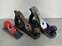 Front angle view of three Stanley hand planes with two larger and one smaller red-bodied plane